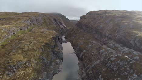 River-flowing-through-steep-canyon-walls-in-Norwegian-highlands,-aerial-view