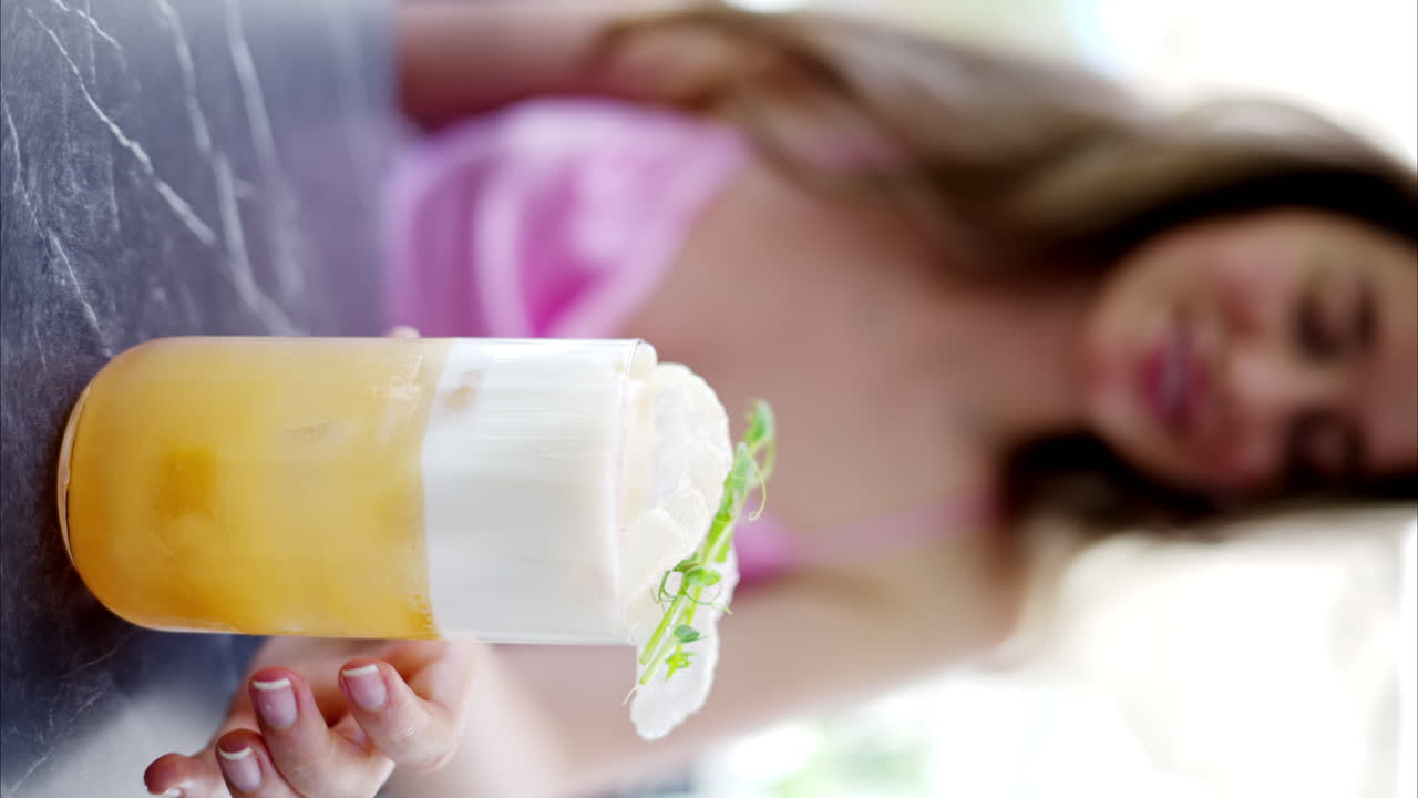 Woman holding a summer white and orange cocktail with whiskey and peach juice, slow motion vertical screen