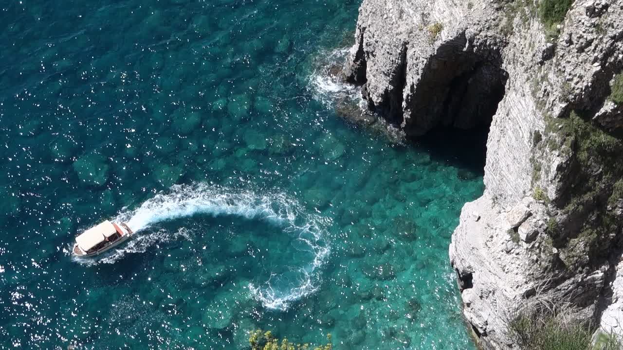 speedboat makes circles on sea water in front of huge cave. Montenegro coastline. High angle view