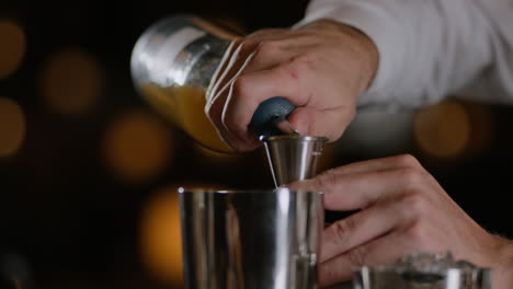 Primer-Plano-De-Un-Barman-Midiendo-Licor-En-Un-Jigger-Y-Vertiéndolo-En-Una-Coctelera-De-Metal.