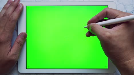 man writing on tablet with green screen chroma key on marble table with stylus