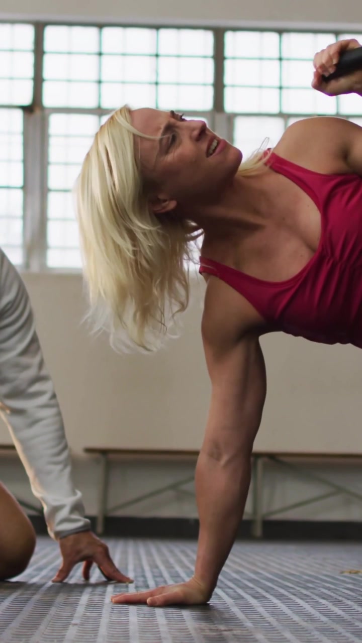Video verticale: Una donna che preme il palmo, ruotando e sollevando un kettlebell per l'allenamento del core vicino a sbarre da palestra che si alzano.