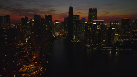 Aerial-descending-footage-of-city-at-night.-Silhouettes-of-downtown-high-rise-apartment-buildings-against-colourful-twilight-sky.-Miami,-USA