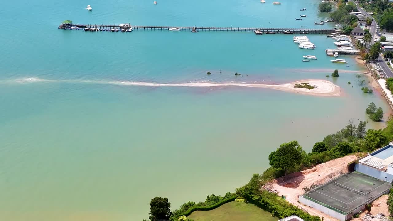 Aerial footage showcasing a pier, sandy coastline, and nearby residential homes with lush greenery.