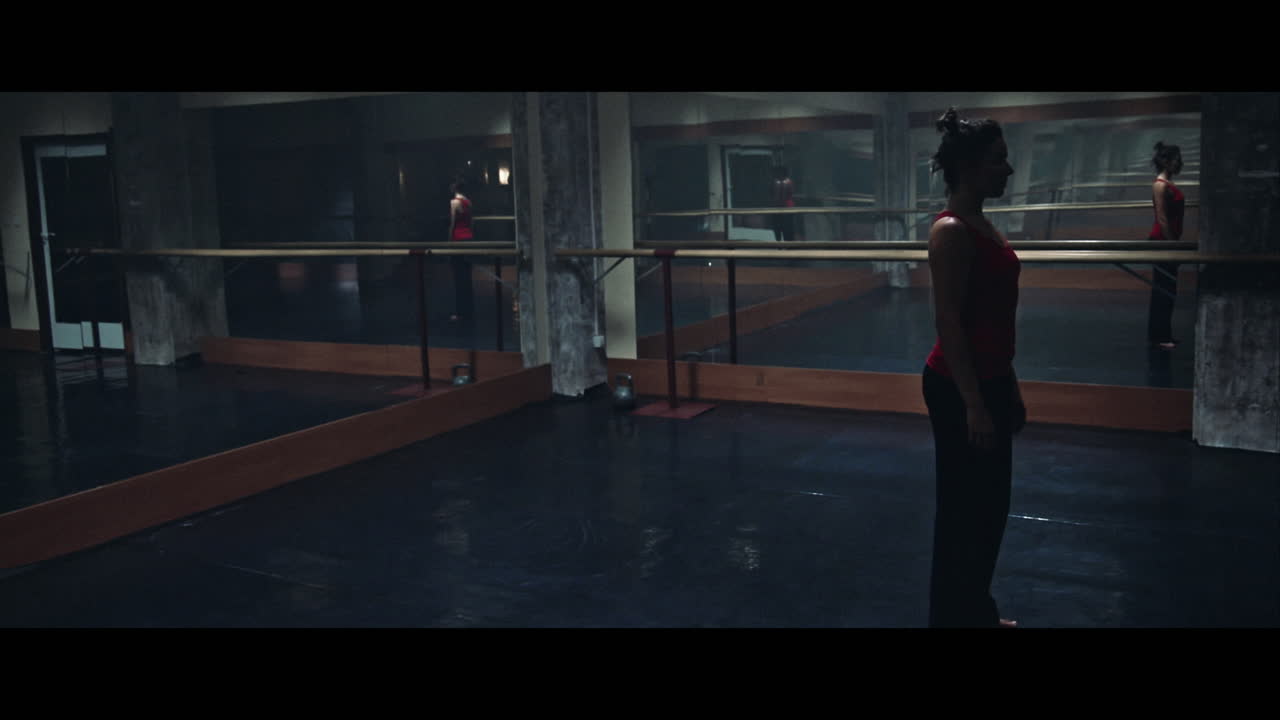 A young woman practices modern dancing and ballet in a moody room full of mirrors