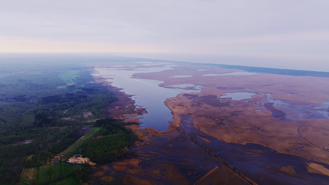 Sweeping drone, Latvia’s Pape Lake, winding shoreline and wetlands, spring haze