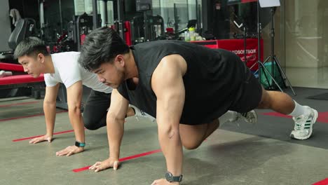 two men perform mountain climbers in a well-lit gym, showcasing strength and endurance. the environment is dynamic and energetic
