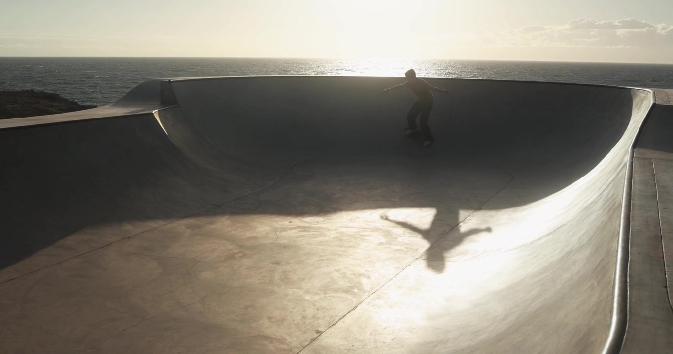 Uomo in skateboard in una bowl di cemento vicino all'oceano al tramonto