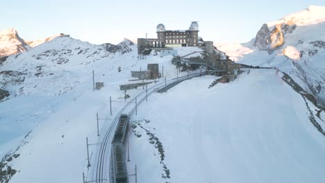 aerial pullback reveals train arriving at gornergrat observation platform in switzerland