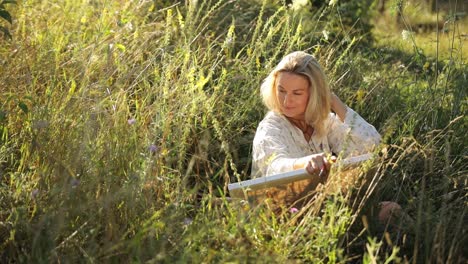 blonde woman relaxing and creating art in a sunny meadow