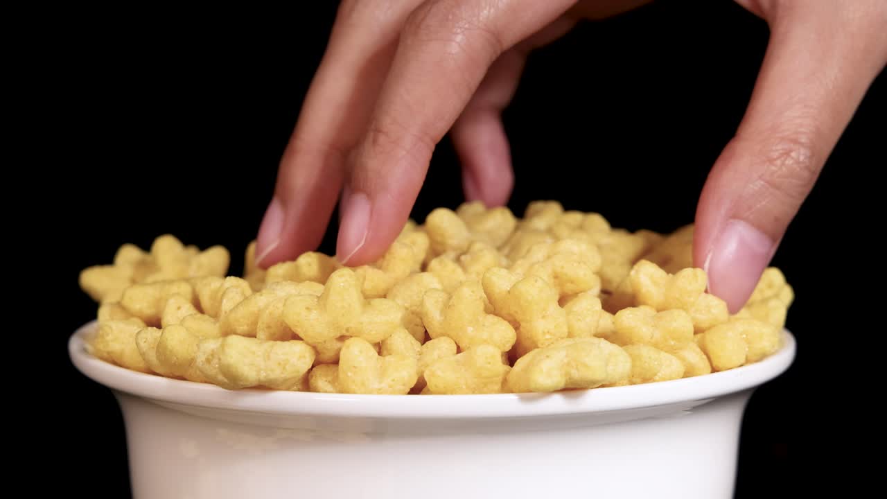 A hand gently stirs cereal in a bowl, captured in slow motion against a black background