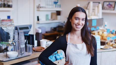 portrait of smiling female owner of coffee shop standing behind counter