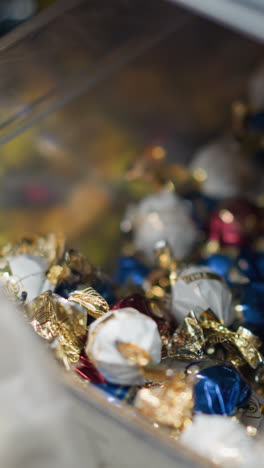 vista de una mano recogiendo dulces de una caja y colocándolos en un paquete en una tienda. filmado con una cámara de mano, capturando la acción de seleccionar dulces de uma variedad de dulces envueltos