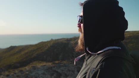 man on top of the mountain facing the sun looking at the horizon with blurry nature background - slow motion