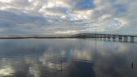 vuelo de drones sobre el agua con reflejos de nubes y vista del puente