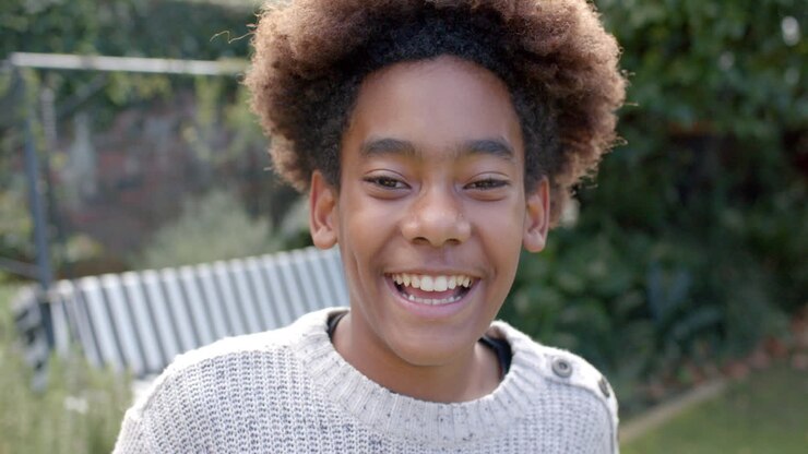 Portrait of happy african american boy looking at camera, smiling in garden, slow motion