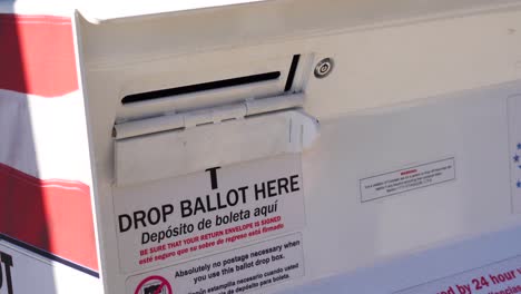 un joven deja caer una carta de votación por correo en la ranura de la urna oficial con el cartel de soltar la papeleta aquí