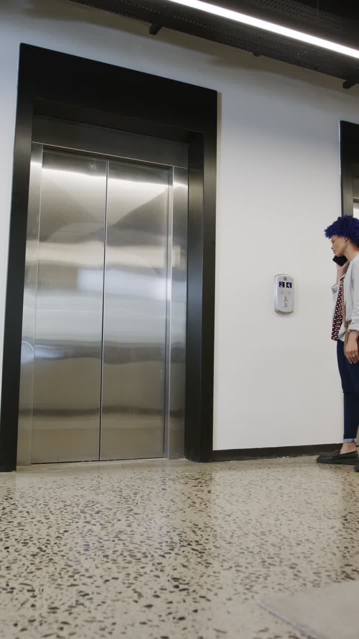 Vertical video of biracial businesswoman talking on smartphone and using elevator, slow motion