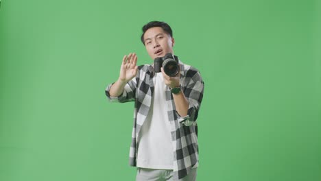 아시아 의 사진작가 가 스튜디오 에서 녹색 스크린 배경 에 있는 카메라 로 사진 을 찍는 동안 왼쪽 과 오른쪽 으로 움직이라고 모델 에게 말 하고 있다