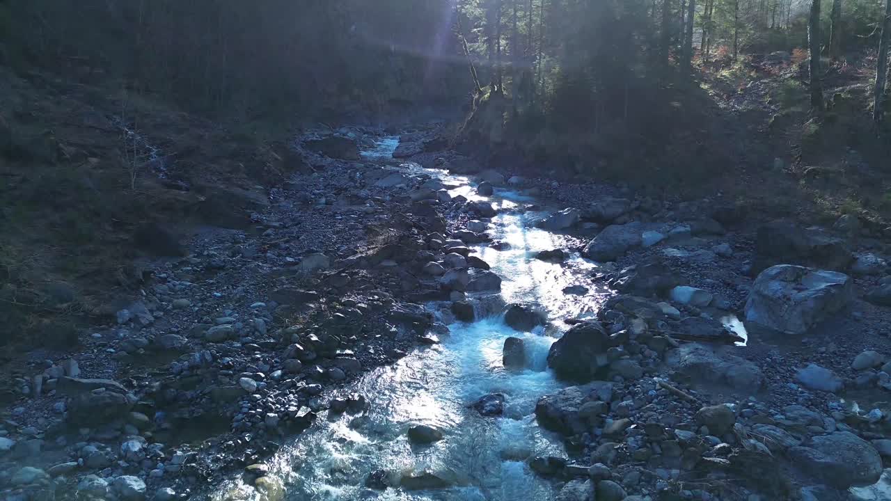 Drone flyver mod sollyset langs en bjergflod i Østrig.