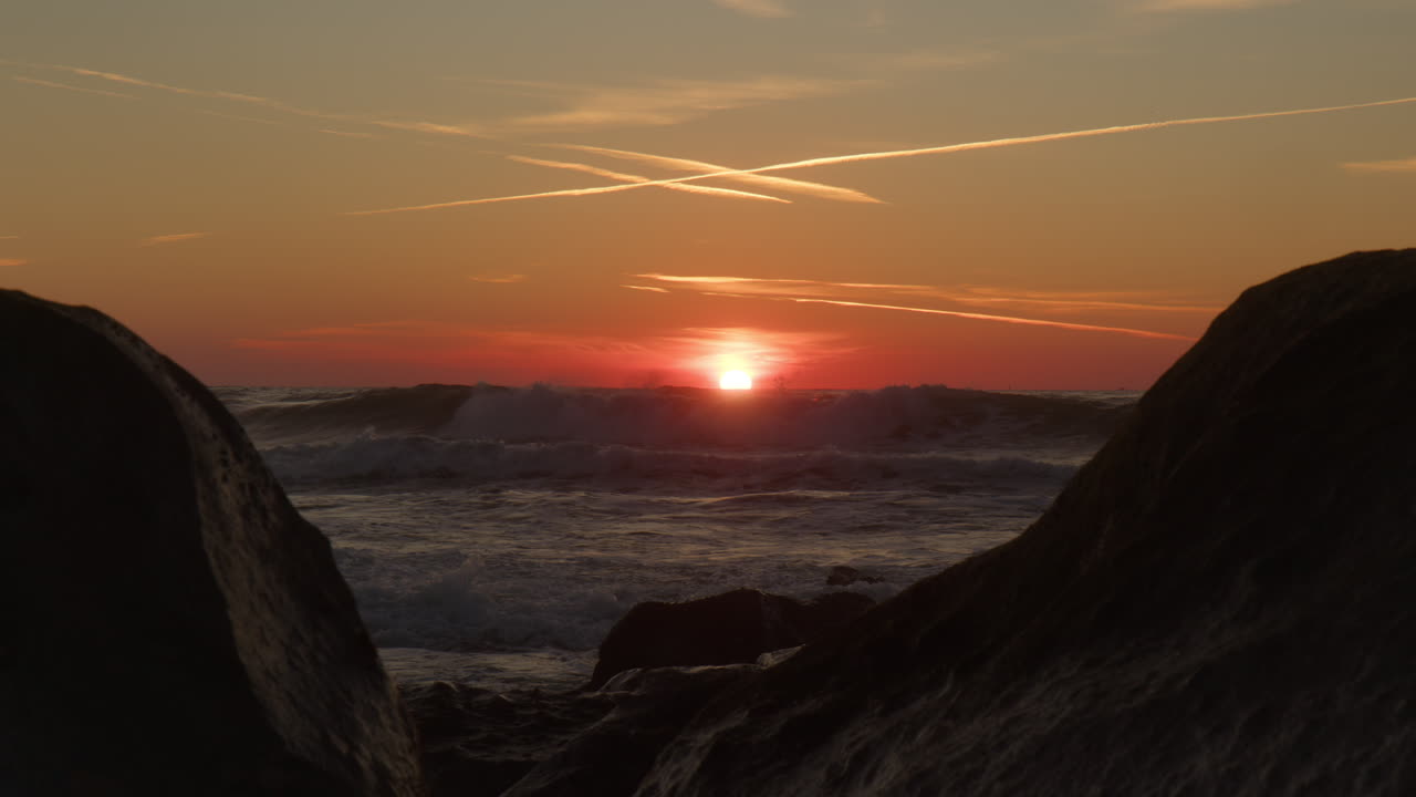 Kraftige havbølger og solnedgang i baggrunden
