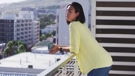 Mixed-race-gender-fluid-person-drinking-cup-of-coffee-on-roof-terrace