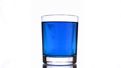 un primer plano de una gota de tinta salpicando en un vaso de agua de color azul.