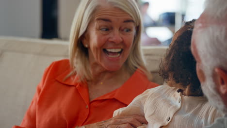 granddaughter cuddling with loving grandparents on sofa at home