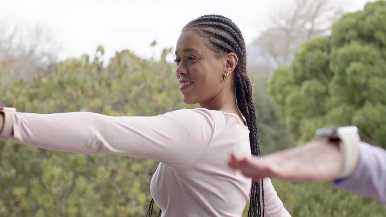 Centering midadult woman in top holding T-pose with friend showing smartwatch on garden balcony