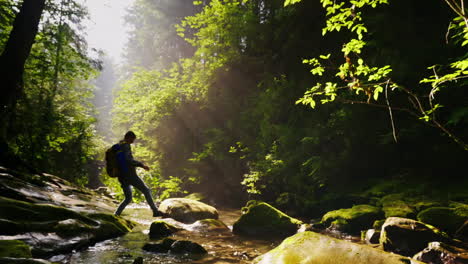 a silhueta de um homem com uma mochila atravessa um rio de montanha ou flui uma bela floresta com raios de