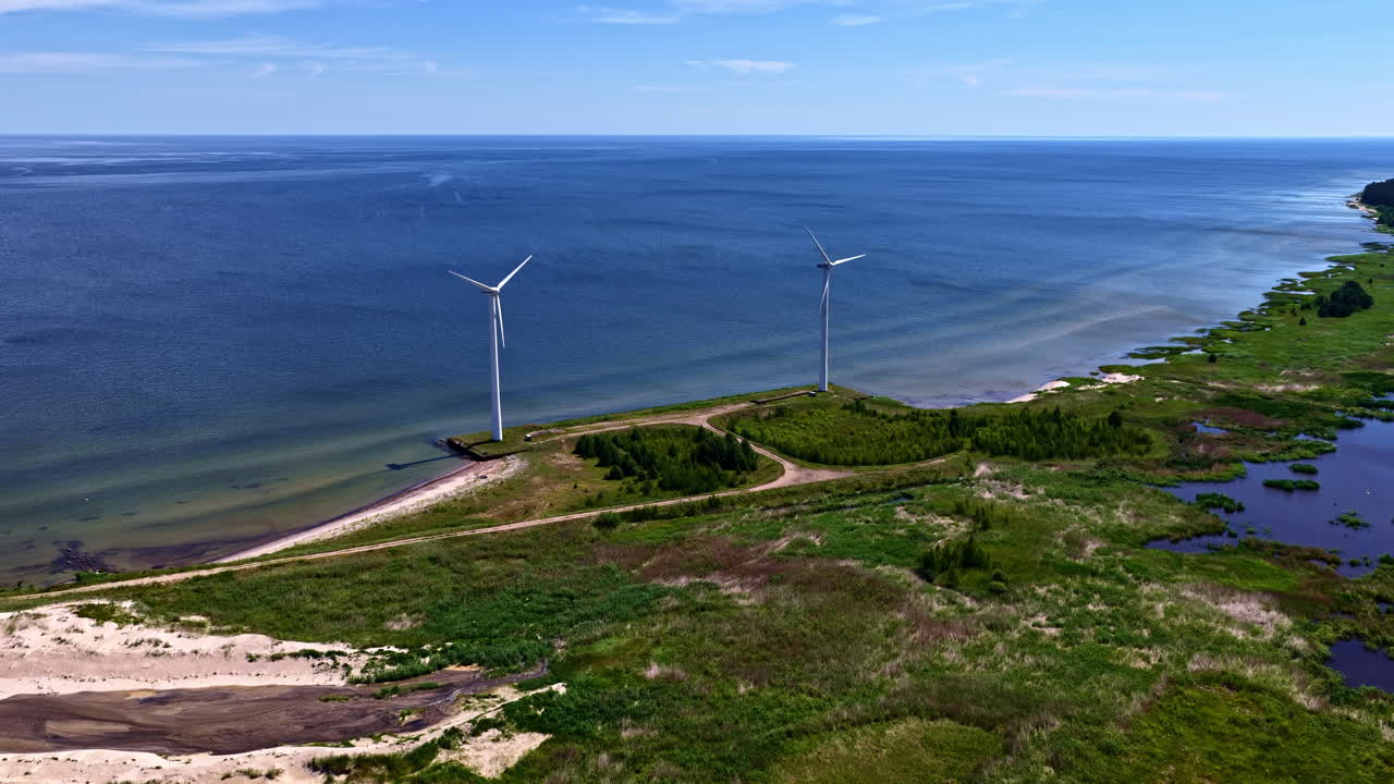 Two wind turbines generating clean, renewable energy, beautifully situated on a narrow coastal peninsula between the Baltic Sea and a lagoon near Engure, Latvia - aerial
