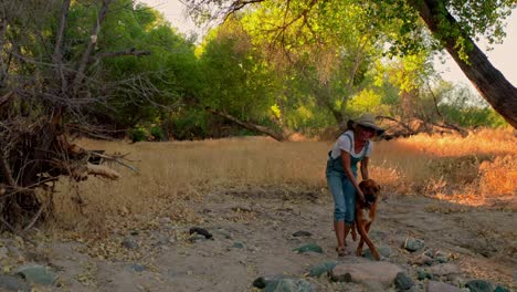 feliz mujer de mediana edad camina y acaricia a su perro a través de la naturaleza del atardecer