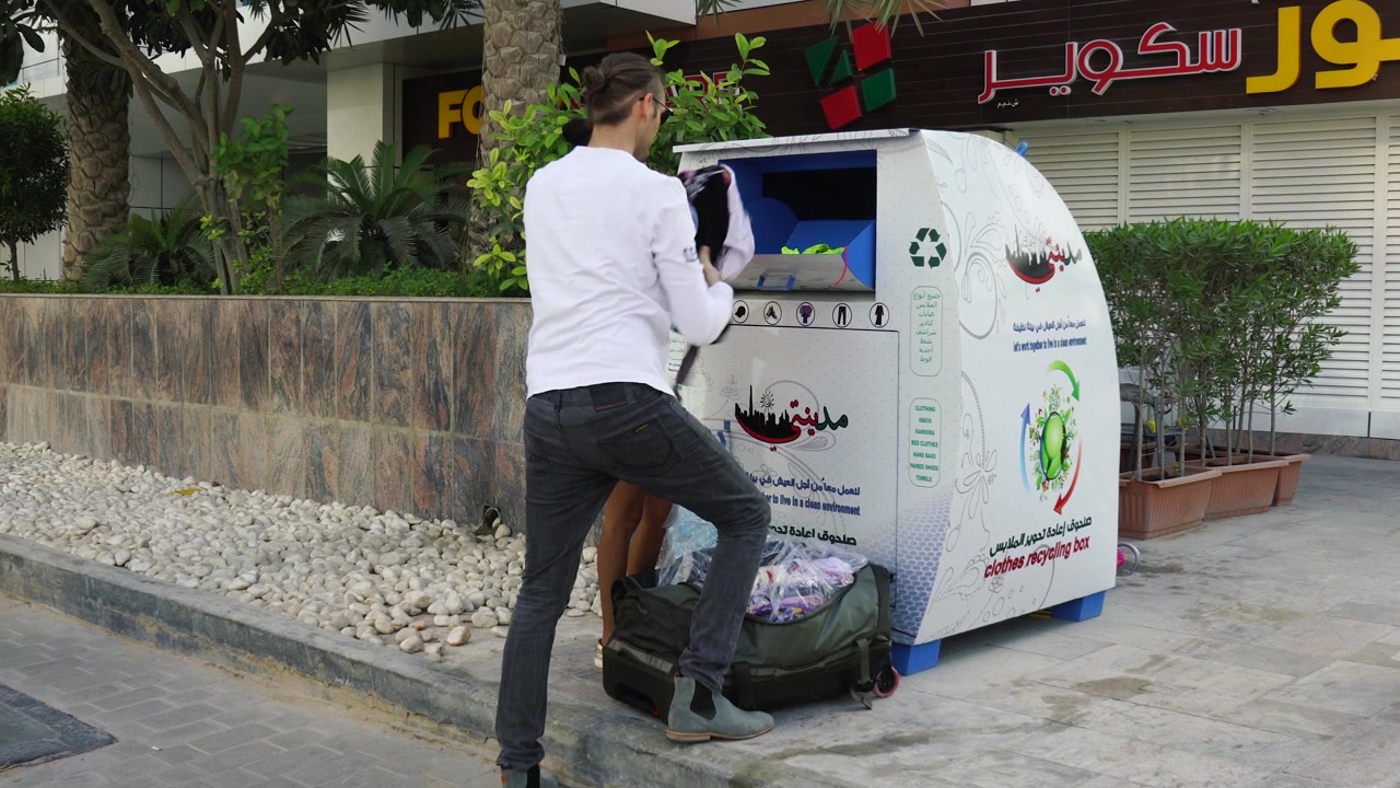 Man and woman donating a load of secondhand clothing to a donation bin on the street in Dubai