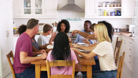 two families with teenage children eating meal in kitchen