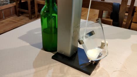 automated cider pour from green bottle into tilted glass using pouring machine indoors