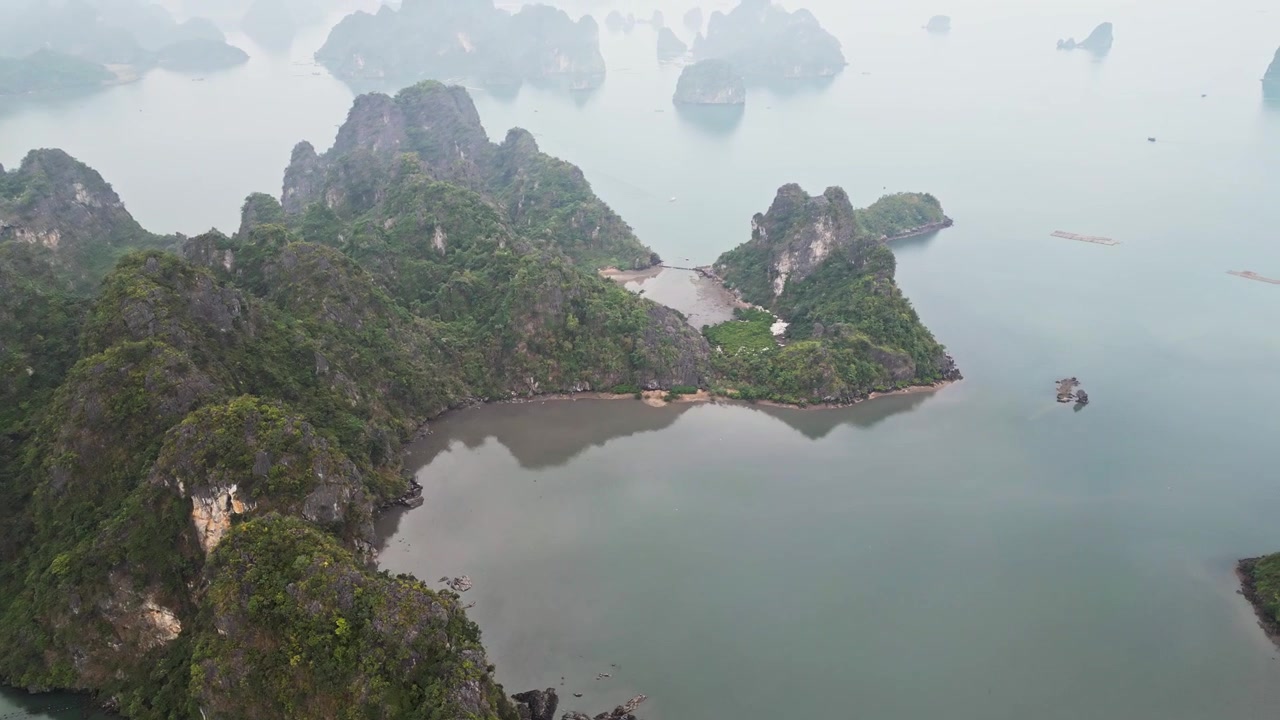 Luftfoto af barske karstøer i Vietnam, omgivet af stille smaragdgrønt vand med frodig vegetation, der dækker stejle kalkstensklipper, og som danner et slående naturligt kystlandskab.