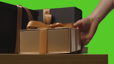 close up of man putting down gift wrapped present in box decorated with ribbon on table shot against green screen