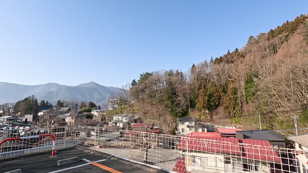 A serene 9-second video capturing a panoramic view of Kawaguchiko, Japan, with mountains and residential rooftops under clear blue skies