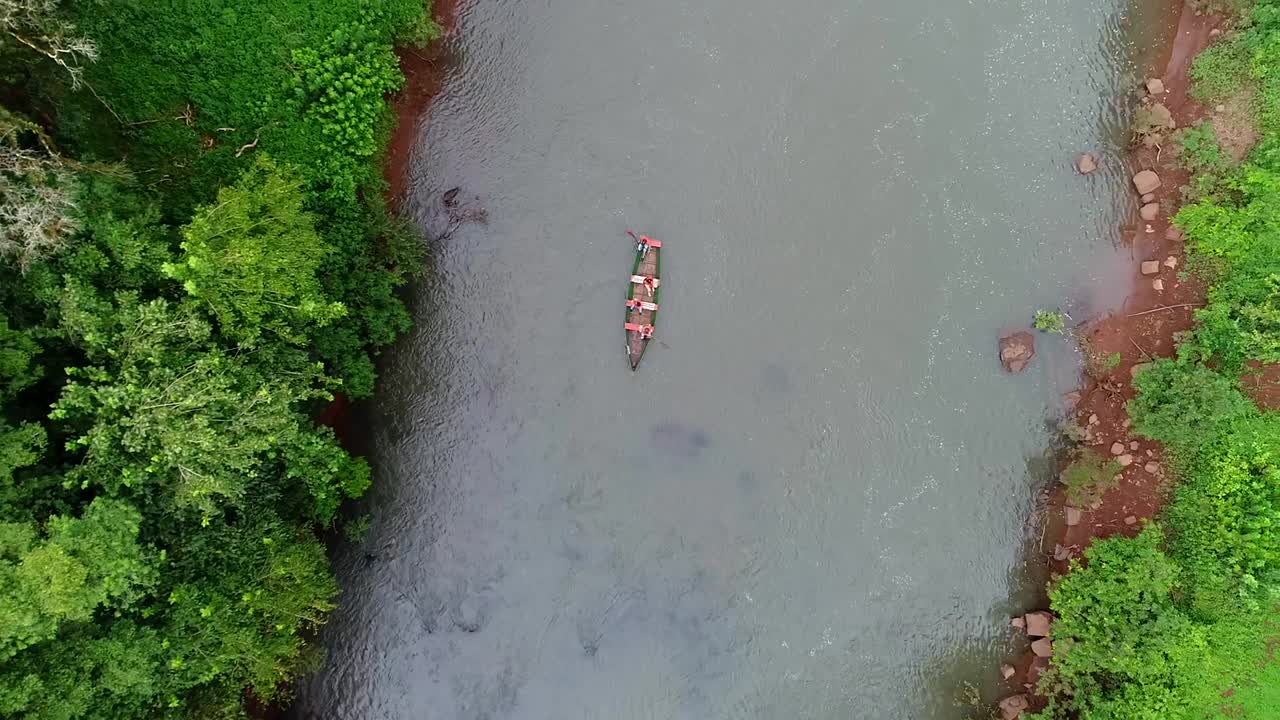 una vista aérea capturada por un avión no tripulado muestra una escena serena de un pequeño bote de remos cruzando pacíficamente un hermoso río en el corazón de la jungla