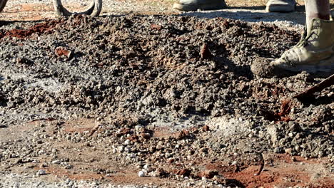 low angle telephoto view of laborer manually mixing concrete with spade