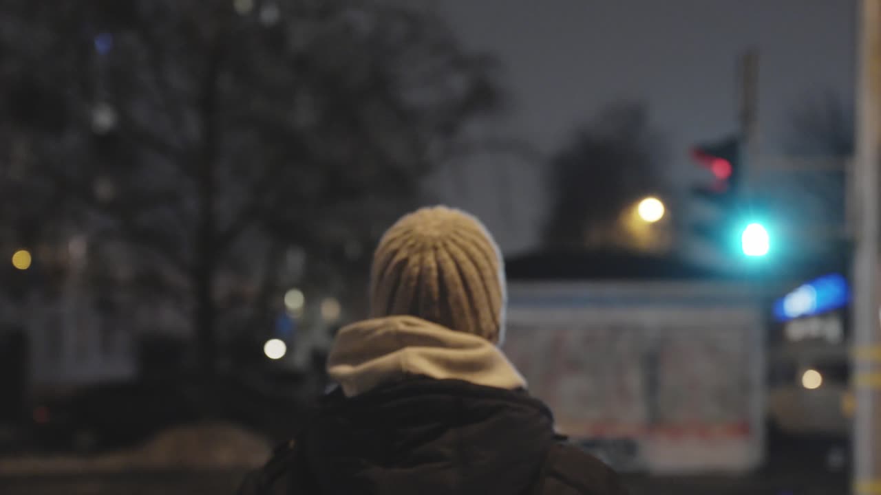 неузнаваемый мужчина в серой шляпе и черной куртке переходит улицу на зеленый свет