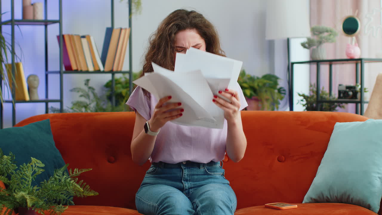 Stressed young woman looking at unpaid bank debt loan, doing paperwork, planning budget throws bills