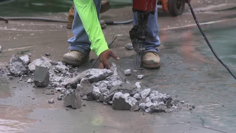 a worker with a jackhammer reaches down to move the rubble and debris away from his work area