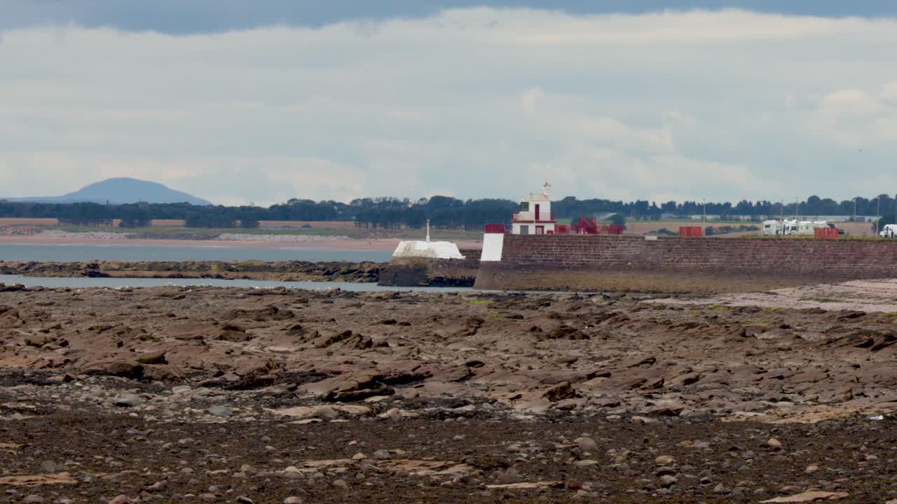 Camera pans from residential buildings to rocky shoreline and lighthouse under overcast daylight