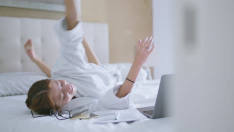 Happy-young-woman-relaxing-on-bed-and-watching-video-on-laptop