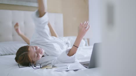 happy young woman relaxing on bed and watching video on laptop