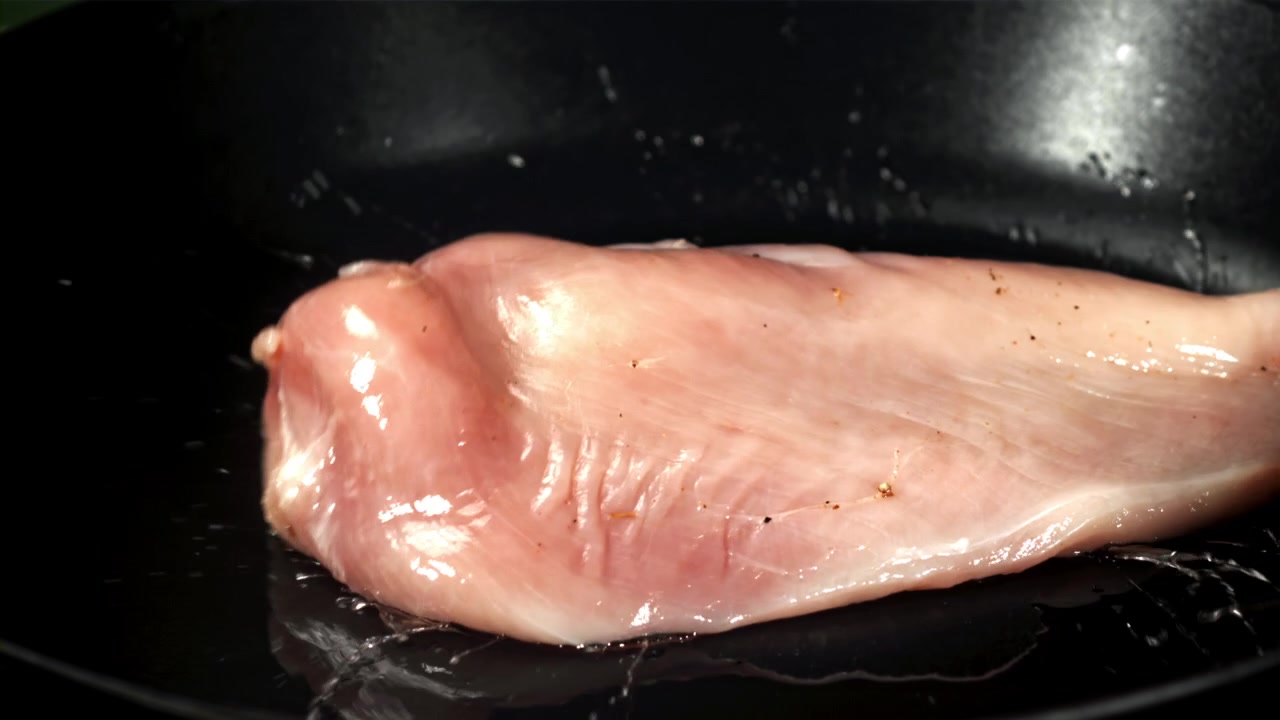 Raw Chicken Breast Sizzling in Hot Frying Pan