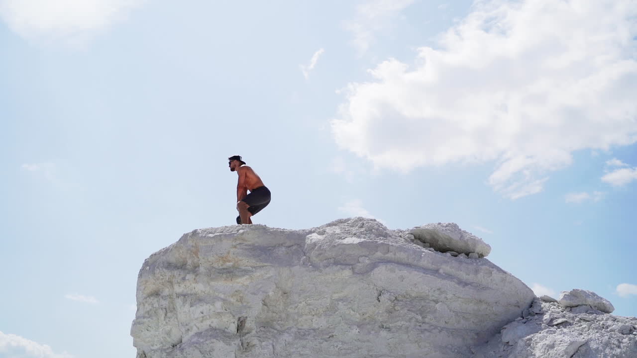 Side view of a strong man lifting kettlebell on white hill. Male athlete swinging kettlebell with two hands on the beautiful natural background outdoors.