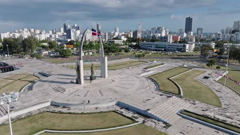 aerial orbit shot of plaza de la bandera in santo domingo with skyline in background