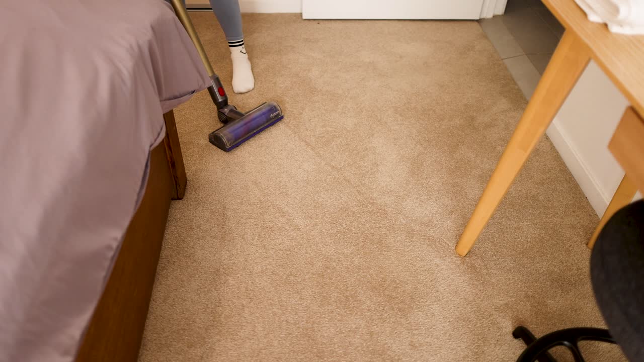 A woman vacuums a carpeted bedroom, showcasing efficient cleaning in a well-lit, organized space